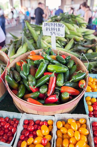 A basket of colorful jalapeno peppers, with grape tomatoes and corn, on display at a farmer's market