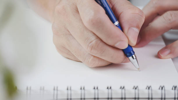 istock Close up hand writing paper on notebook with blue pen to note, memo, list action plan at office or home desk, selective focus. Concept of write on paper, letter, pen, notepad, diary 1409313429