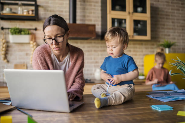 istock Mother in glasses working on laptop computer from home and while baby son sitting on table nearby. Working mom with toddler. Elder daughter playing tablet in background 1409313523