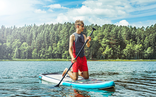 Stand up paddle with a view, young man, teenager on SUP looking at forest. Guy enjoying outdoor activities on  lake