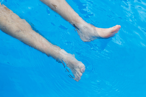 Detail of a man, just feet in swimming pool with nice reflections on water