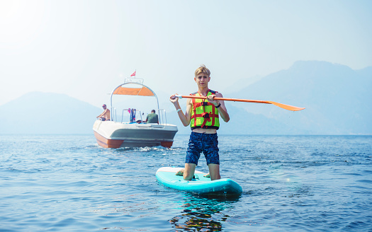 Inflatable stand-up paddle board. Teen in life jacket costs on a sap board looking at the camera.