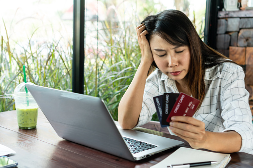 Close up of upset young Asian woman close her eyes while holding credit card with feeling stressed and broke. financial problem, debt concept.