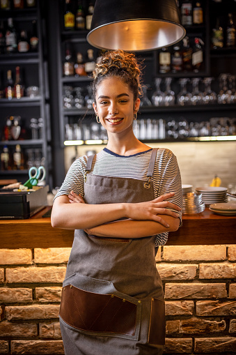 Photo of woman barista standing at the bar counter in coffee shop and looking at camera.