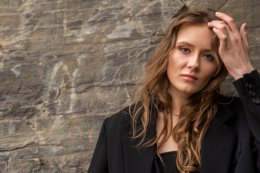 Headshot of serious young mixed race female wearing dark business suit looking at camera, her eyes full of distrust and disappoinment as she has quarrel with boyfriend, standing at wall