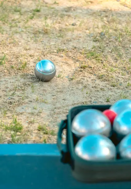 Photo of Invitation to petanque game concept, no people. Metal balls and cochonnet set blurred in foreground, focus on ball in background on sandy area with sparse grass. Sunny summer team building,copy space