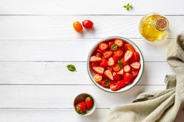 салат из томатной черри и клубники, украшенный листьями базилика - strawberry tomato стоковые фото и изображения