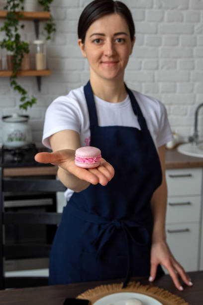 Pink macaroon is lying on woman's palm. Selective focus. Image for website about desserts, food, and confectionery. stock photo