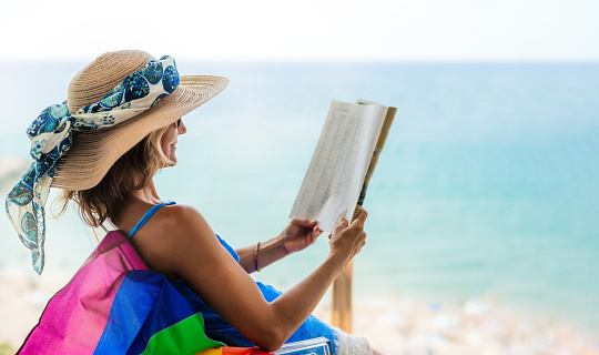 woman lying on beach and reading, sunset time, at the edge of sea, sunhat.photo taken in summer day outdoors.