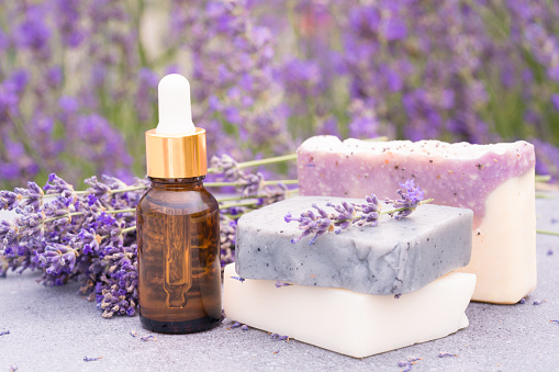 Lavender beauty products - cosmetic oil or face serum and natural handmade soap bars against lavender flowers field as background with copy space. Herbal cosmetics
