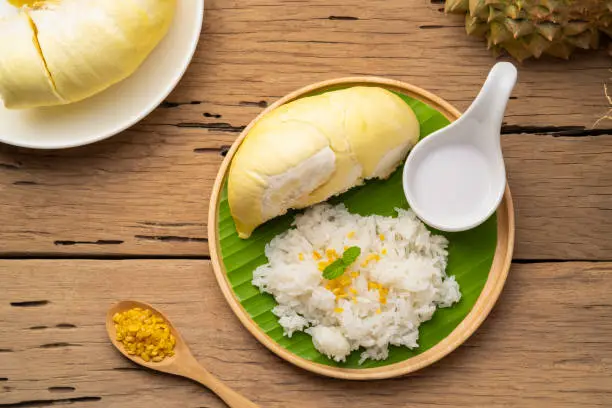 Cooked sweet glutinous rice topped with yellow bean and durian fruit,served with sweet coconut milk on wooden plate.Top view