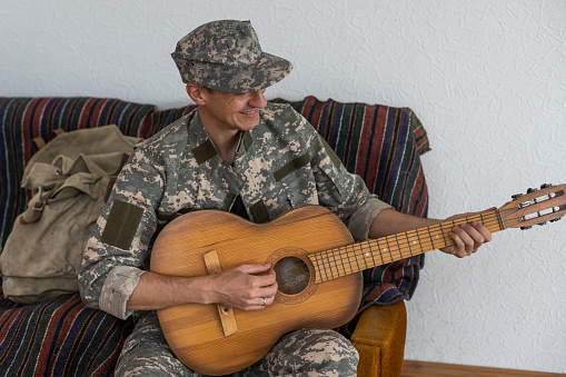Veteran In The Wheelchair Guitar Play Concept. Family Meeting. Son And Wife. Camouflage Uniform. Family Background. Resting Together. Feelings Showing. Patriotic Comeback. Paralyzed Soldier.
