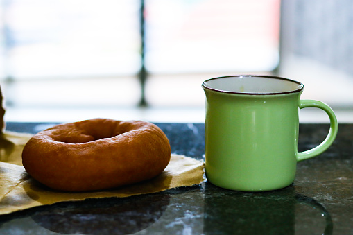 Photo of a fresh donut with a green hot drink mug, sat on a granite countertop, tight focus, dark