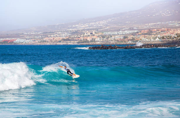 surfer girl on a ocean wave against the background of costa adeje, spain. - image alternative energy canary islands color image imagens e fotografias de stock