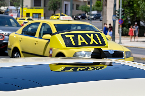 Athens, Greece - May 2022: Close up view of the sign on the roof of a taxi cab in the city centre, with reflection in the sunroof, and another taxi in the background
