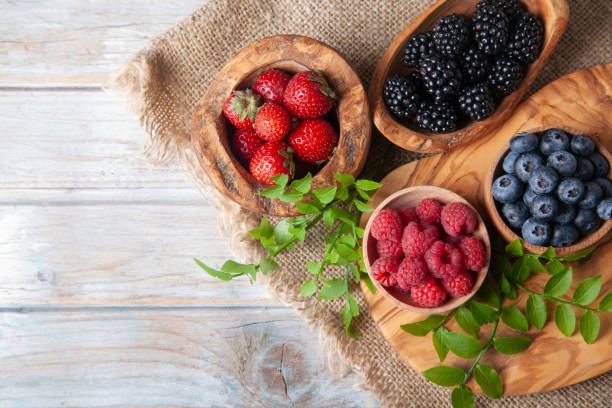 bunte beeren-sortiment auf rustikalem holztisch - beere pflanzenbestandteile stock-fotos und bilder