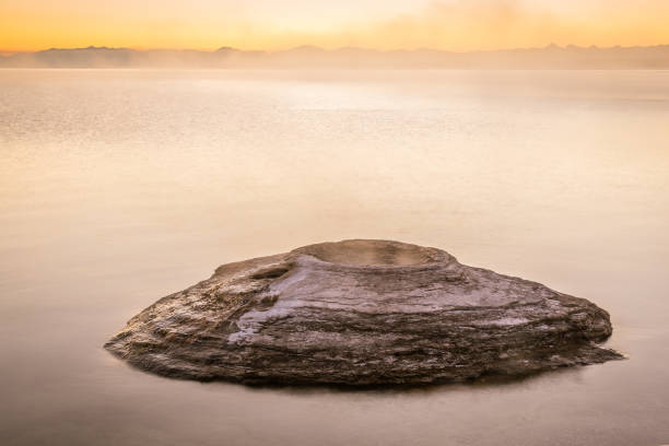 iconic fishing cone at sunrise in west thumb geyser basin with lake yellowstone in background, yellowstone national park - natural basin imagens e fotografias de stock