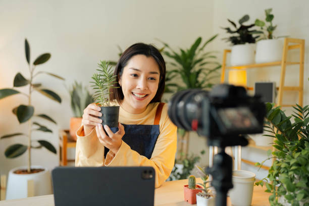 mulher asiática ao vivo transmitindo pela câmera para vender plantas em casa. - women home video camera camera vitality - fotografias e filmes do acervo