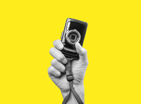 Man hand holding point and shoot camera. Black and white image on yellow background. Practical and compact digital device for taking photos in photographer arm.