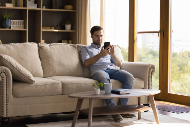 istock Millennial man wearing wireless headphones relaxing on sofa using phone 1409343479