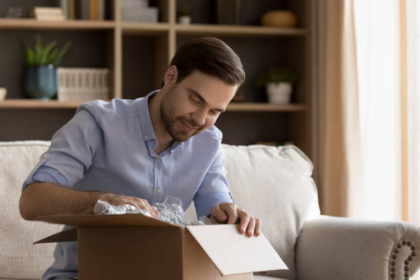 istock Curious young male unpack cardboard box parcel got by mail 1409343482