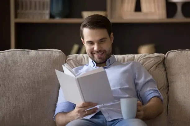 Photo of Young man reader holding cup of coffee enjoying favorite book