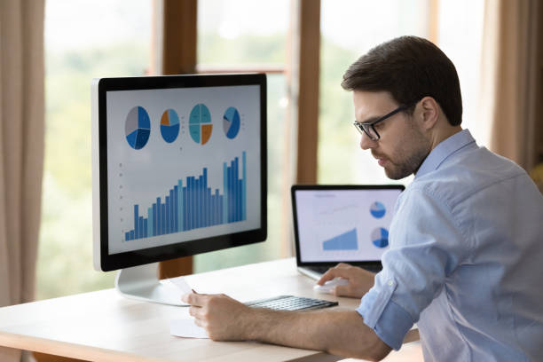 istock Serious young businessman work with infographic on laptop desktop computers 1409343566