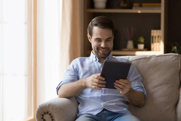 istock Happy millennial male rest on couch watch video on touchpad 1409344311