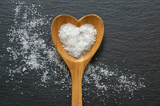 White salt in heart shaped spoon on black table. Copy space