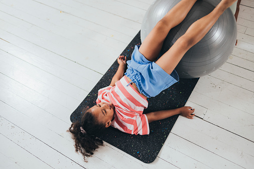 Young Latin girl exercising on a mat, using a pilates ball.
