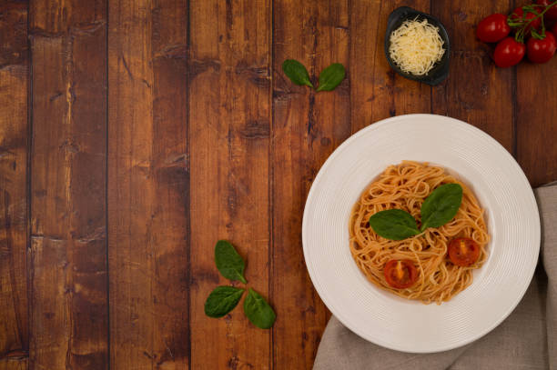 Spaghetti with tomato sauce, fried cherry tomatoes, grated cheese and basil leaves on a brown wooden table top. Top view.