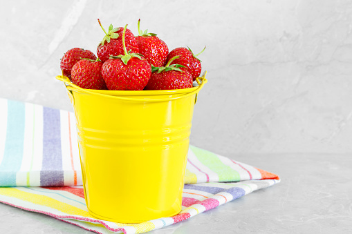 Juicy ripe tasty strawberries in  yellow metal bucket with striped towel on stone countertop. Summer harvest