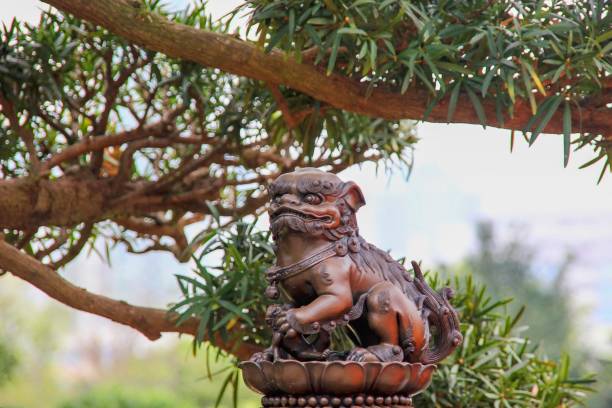 kleine schöne statue des mythischen chinesischen löwenwächters auf verschwommenem astbaumhintergrund im chi lin nunnery park, hongkong. chinesische kaiserliche schutzlöwen sind traditionelle chinesische architekturornamente. - chinese temple dog stock-fotos und bilder