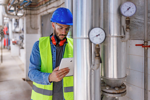 A young Caucasian male engineer is checking the manometers and holding a tablet.