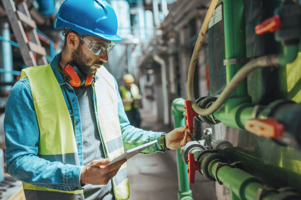 Checking everything twice A young Caucasian male engineer is examining the pipe system and checking the data on his tablet. switchboard operator stock pictures, royalty-free photos & images