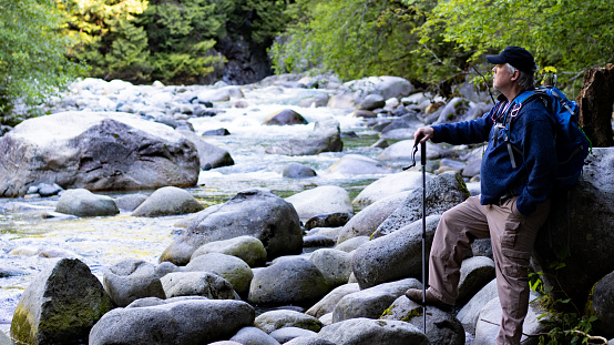 Old man with hat sitting meditates in front of a stream