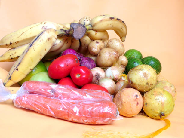 istock Yellow onions, red onions, lemons and potatoes inside net packets, with three more ripe tomatoes and a green tamate, mananas, oranges on a yellow background 1409372694