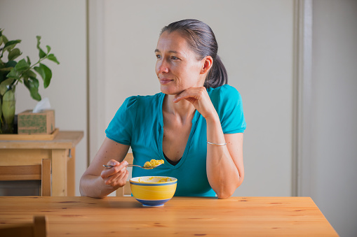 Smiling woman eating healthy kitchari for a breakfast. Indian cuisine. Lifestyle portrait.