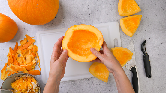 Peeled raw pumpkin slices close up on cutting board, flat lay, grey stone background, woman hands