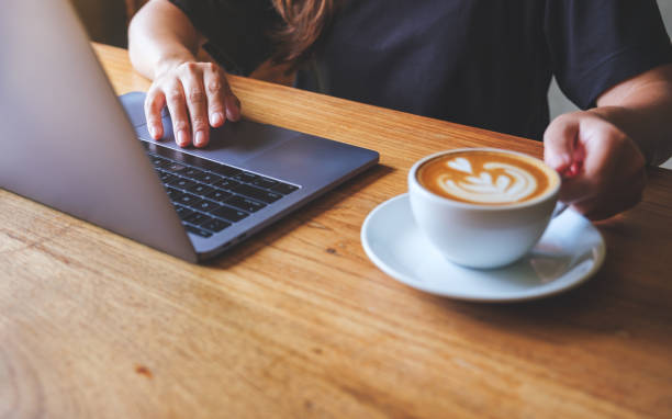 istock Closeup image of a woman holding and drinking hot coffee while working on laptop computer 1409392948