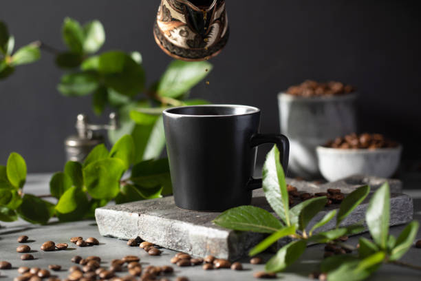 istock Coffee is poured into a black mug from a metal cup on a dark background. 1409399022