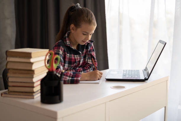 istock Little student sit at desk at home look at laptop screen studying and making notes, concentrated Caucasian schoolgirl watch webinar on computer, home distance education, homeschooling 1409399650