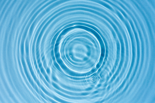 Abstract blue water background with round ripples, closeup. Blue water backdrop. Summer background with drops. Cosmetic and spa concept