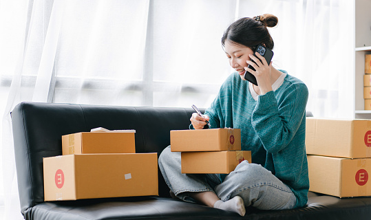 Portrait of a small business startup, SME owner, female entrepreneur, working, unboxing, checking orders online. To prepare to pack boxes for sale to SME customers online business ideas