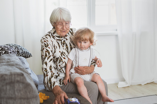 Elderly woman with her little grandson playing at home on the sofa