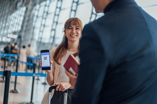 An Asian Chinese woman showing online boarding pass on her smart phone screen at the airport departure area.