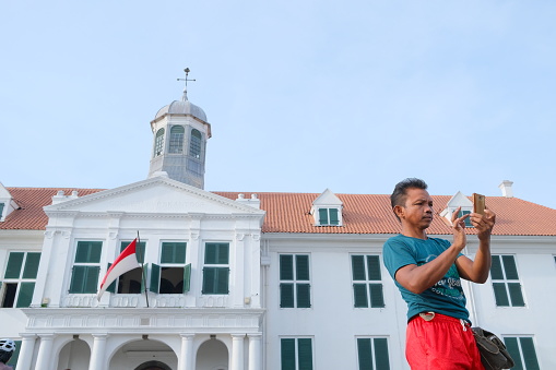 Jakarta, Indonesia - June 12, 2022: Asian man takes a selfie in front of the Fatahillah Museum in the old city of Jakarta.