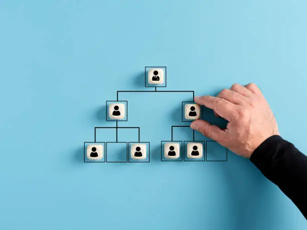 Photo of Male hand arranges company hierarchical organizational chart of wooden cubes on blue background.