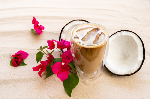 Iced coffee with milk and coconut on sand beach.