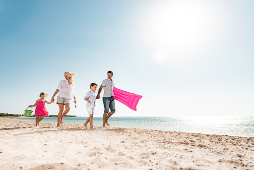 Low angle view of smiling family walking on the beach in summer day. Copy space.